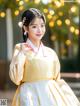 A woman in a yellow and white hanbok poses for a picture.