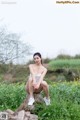 A woman sitting on a tree stump in a field.