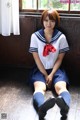 A woman in a school uniform sitting on the floor.