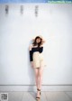 A woman standing in front of a white wall wearing a straw hat.