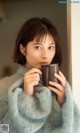 A woman in a blue sweater holding a cup of coffee.