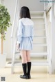 A woman in a blue and white shirt and skirt standing in front of stairs.