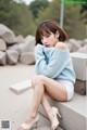 A woman sitting on a concrete ledge wearing a blue sweater and white shorts.