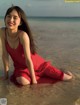 A woman in a red dress sitting on the beach.