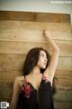 A woman in a black dress leaning against a wooden wall.