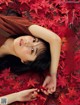 A woman laying on the ground surrounded by red leaves.